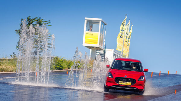 Ein rotes Auto weicht einer Wasserfontäne auf einer Piste in einem Fahrtechnik Zentrum aus