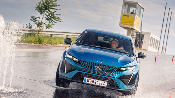 Ein älterer Herr am Steuer eines blauen Autos weicht einer Wasserfontäne bei einem Fahrsicherheitskurs aus