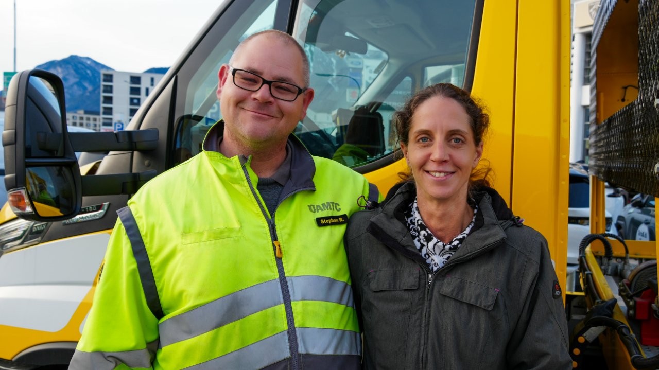 Auf dem Bild sieht man einen Mann in ÖAMTC Uniform der gemeinsam mit seiner Frau vor einem gelben LKW steht.