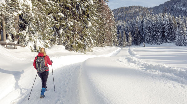 Ein Wanderer geht mit Wanderstöcken auf einem verschneitem Weg.