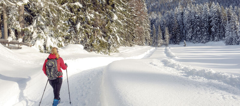 Ein Wanderer geht mit Wanderstöcken auf einem verschneitem Weg.