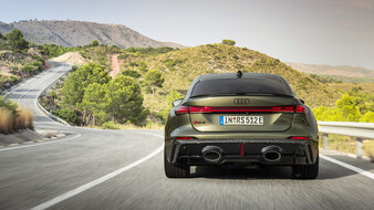 Heck eines dunkelgrünen Audi RS 5 als Limousine, das über eine kurvige Bergstraße fährt.