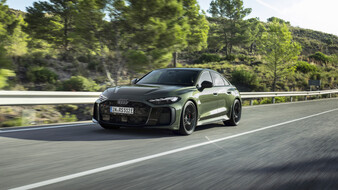 Ein dunkelgrüner Audi RS 5 Avant als Limousine fährt auf einer Landstraße an Bäumen vorbei.