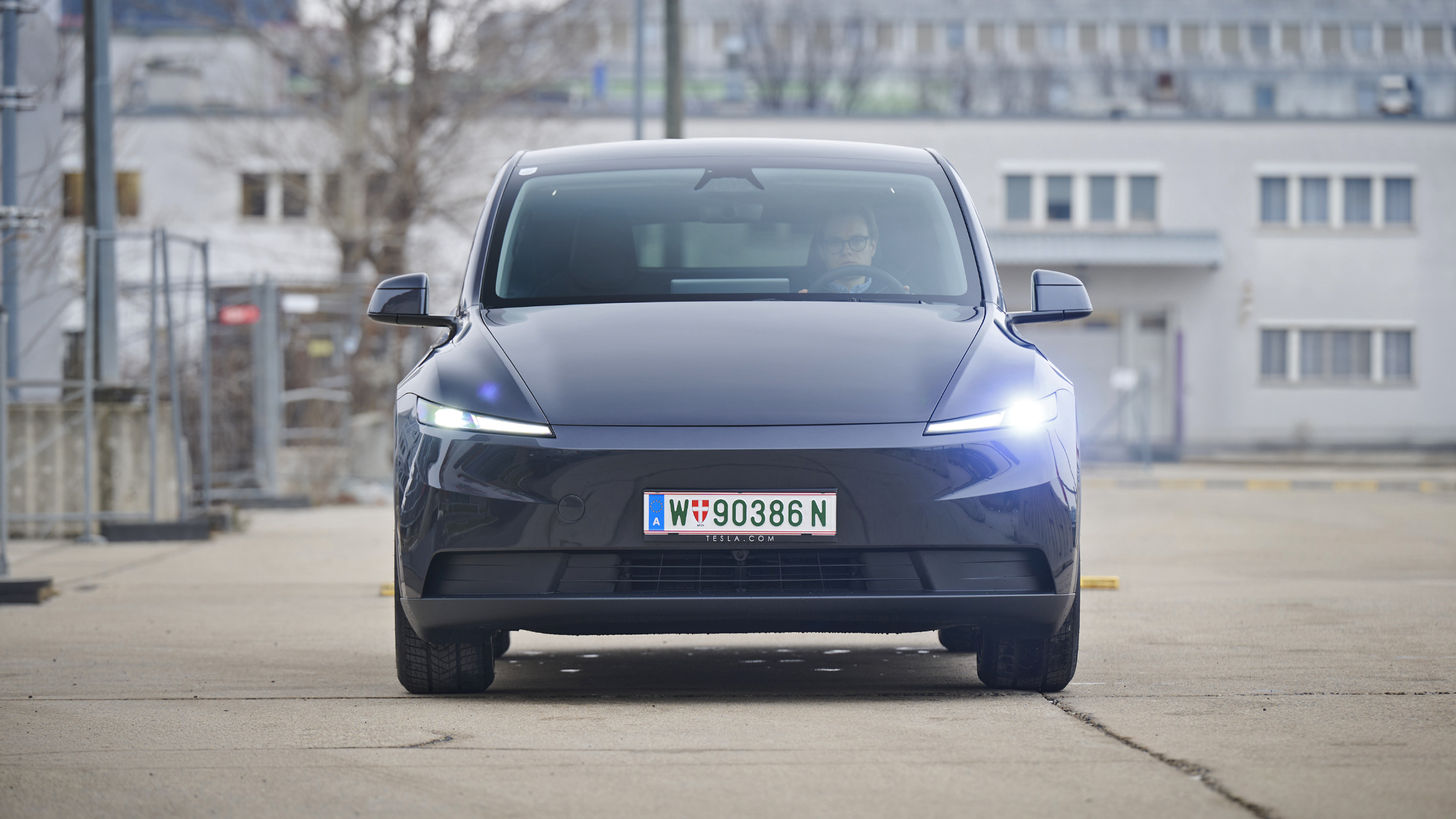 Ein dunkelgrauer Tesla Model Y steht auf einer Straße vor einem hellgrauen Gebäude.