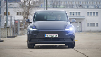 Ein dunkelgrauer Tesla Model Y steht auf einer Straße vor einem hellgrauen Gebäude.