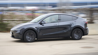 Ein dunkelgrauer Tesla Model Y fährt auf einer Straße.
