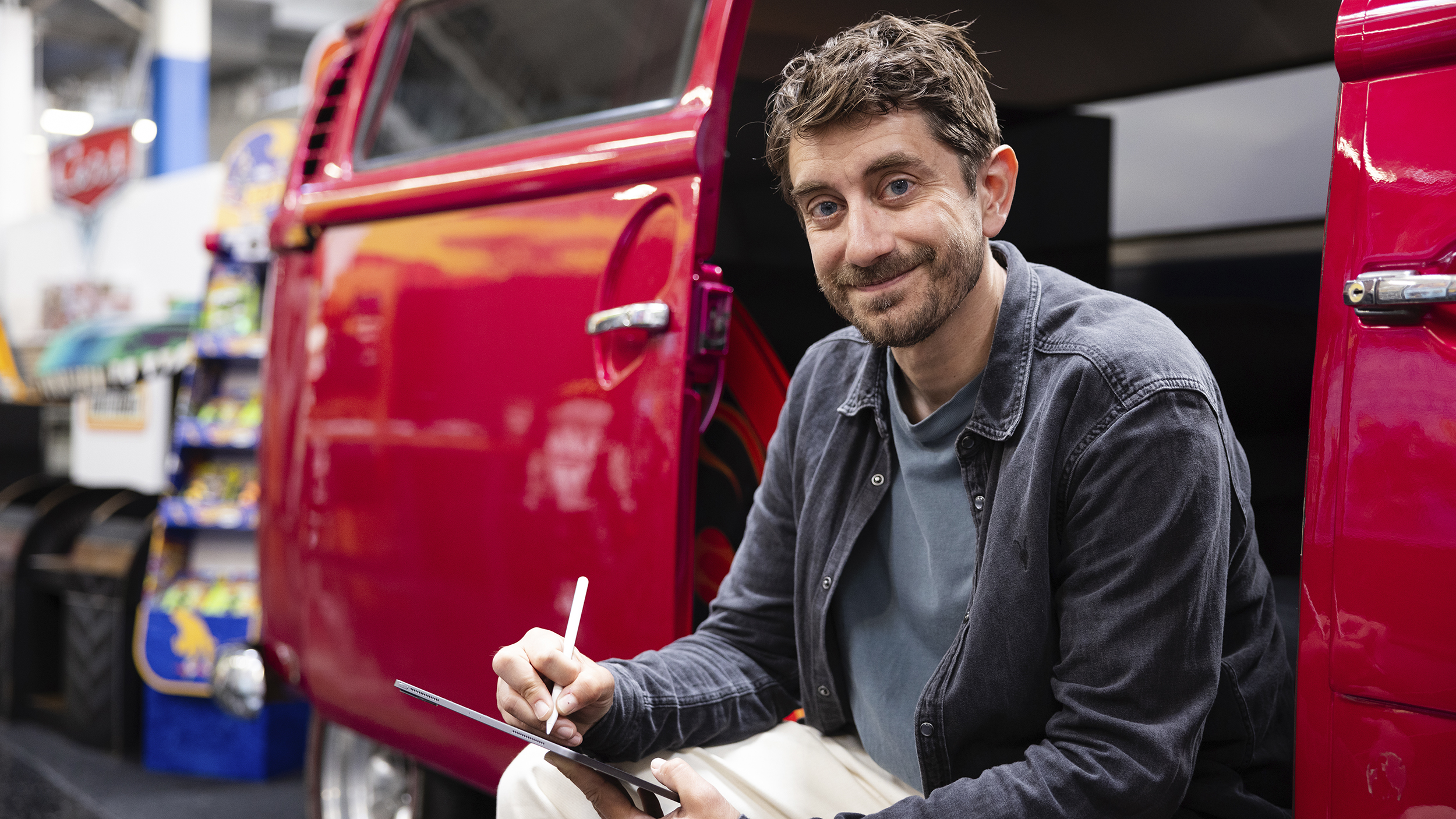 Craig Callum sitzt seitlich in einem alten roten VW Bus und blickt in die Kamera
