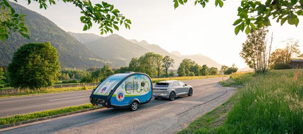 Es ist ein Straße bei Sonnenuntergang zu sehen. Es fährt ein Auto mit dem ÖCC-Campinganhänger.