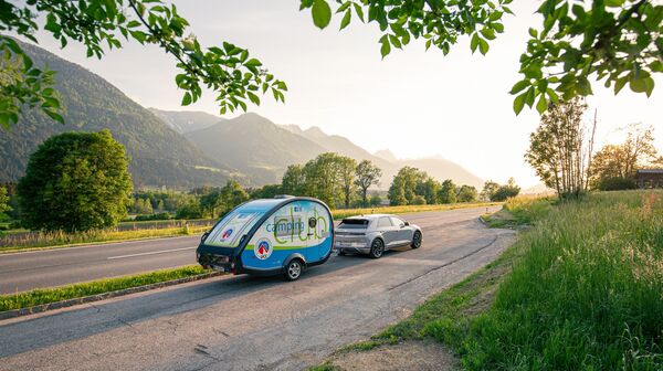 Es ist ein Straße bei Sonnenuntergang zu sehen. Es fährt ein Auto mit dem ÖCC-Campinganhänger.