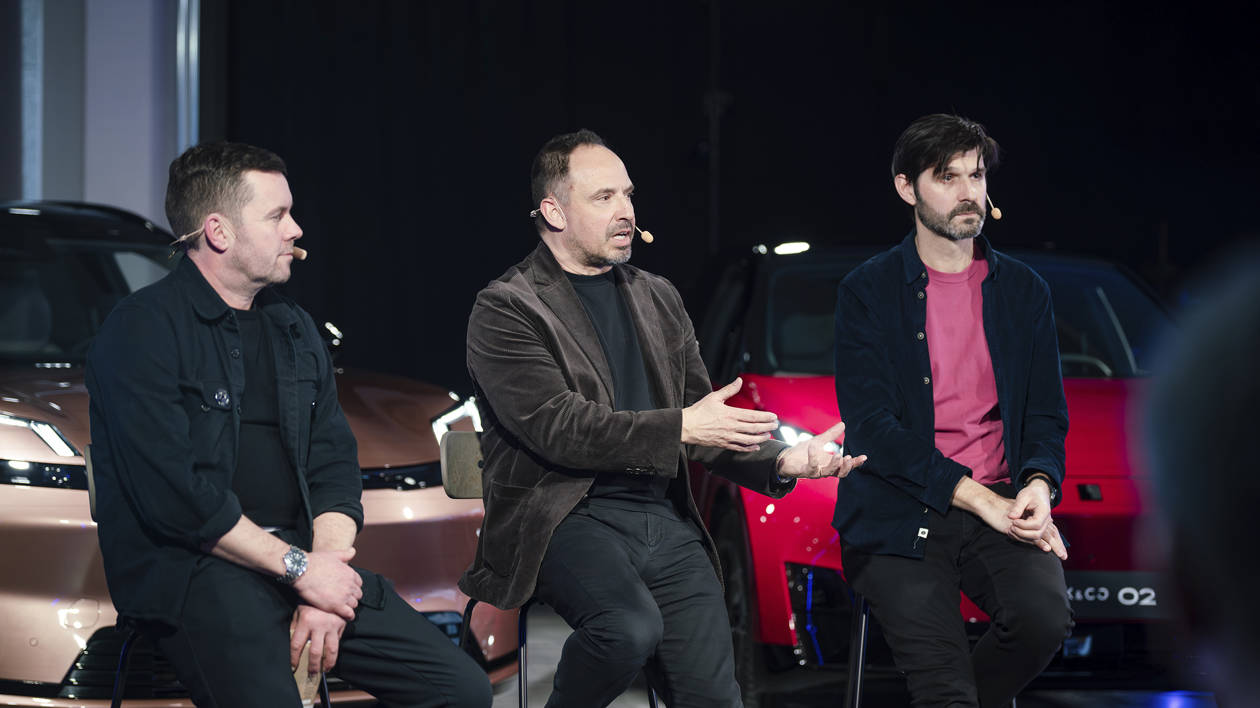 Drei Personen sitzen bei einem Q&A auf Hockern vor drei Fahrzeugen.