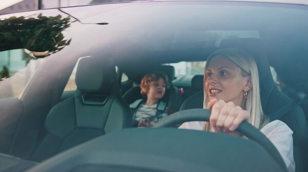 Eine blonde Frau am Steuer eines Autos, am Rücksitz sitzt ein Kind.