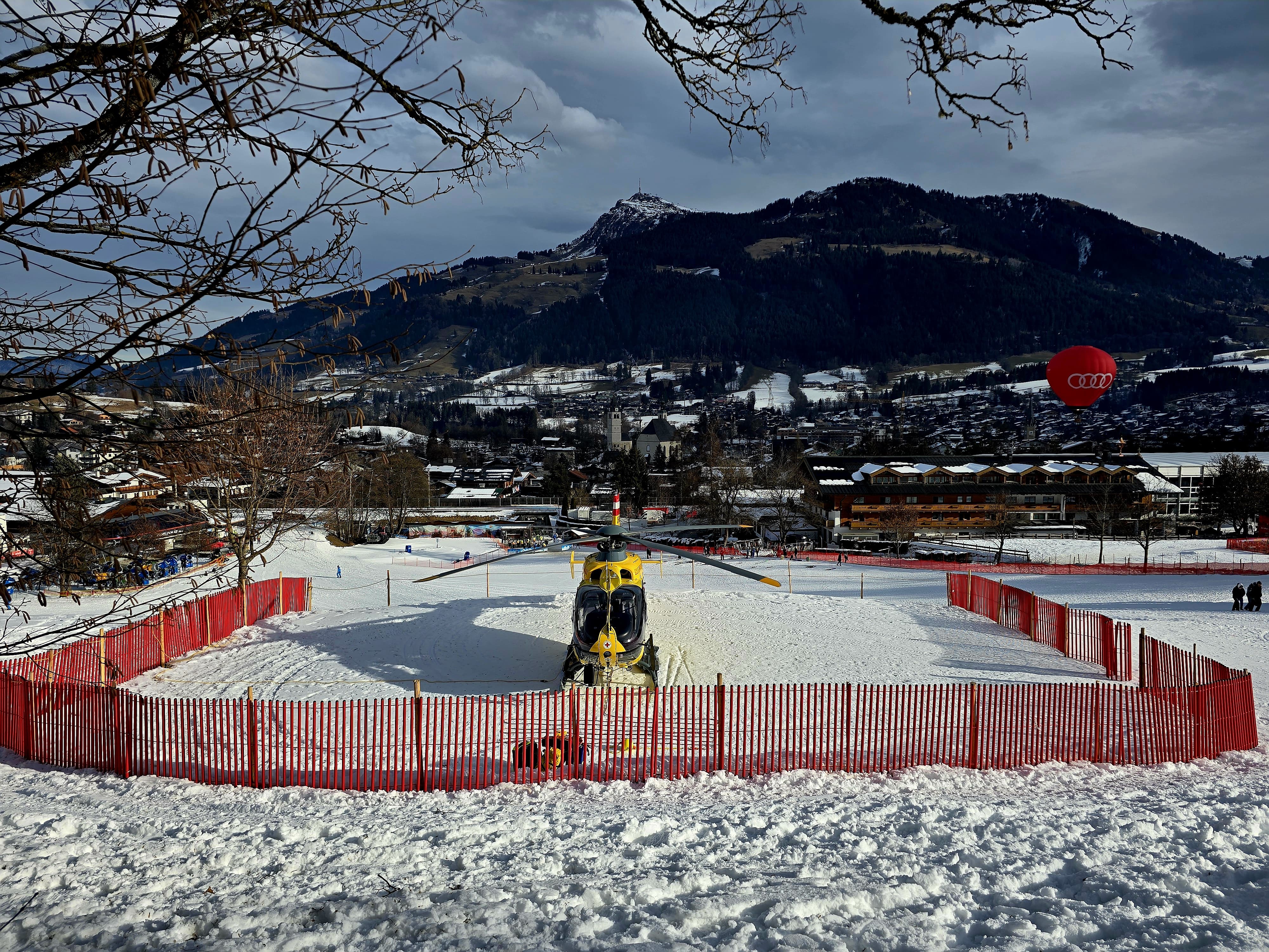 Auf dem Bild sieht man einen gelben Hubschrauber, der in einem abgegrenzten Bereich in einer Winterlandschaft steht.