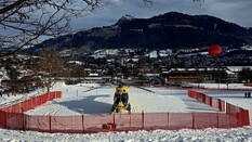 Auf dem Bild sieht man einen gelben Hubschrauber, der in einem abgegrenzten Bereich in einer Winterlandschaft steht.