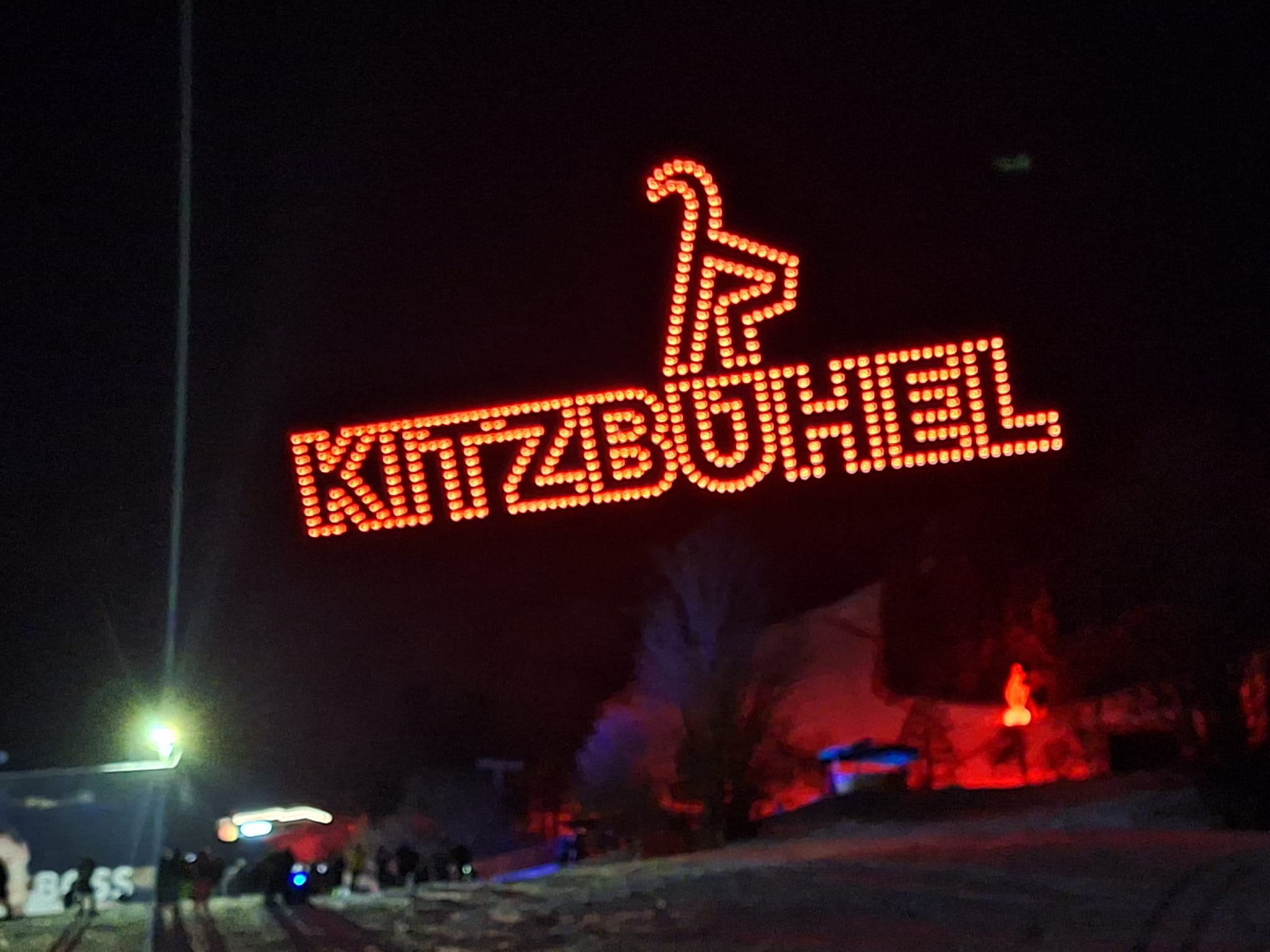Auf dem bild sieht man farbige Drohnen vor einem Nachthimmmel, die das Wort Kitzbühel schreiben