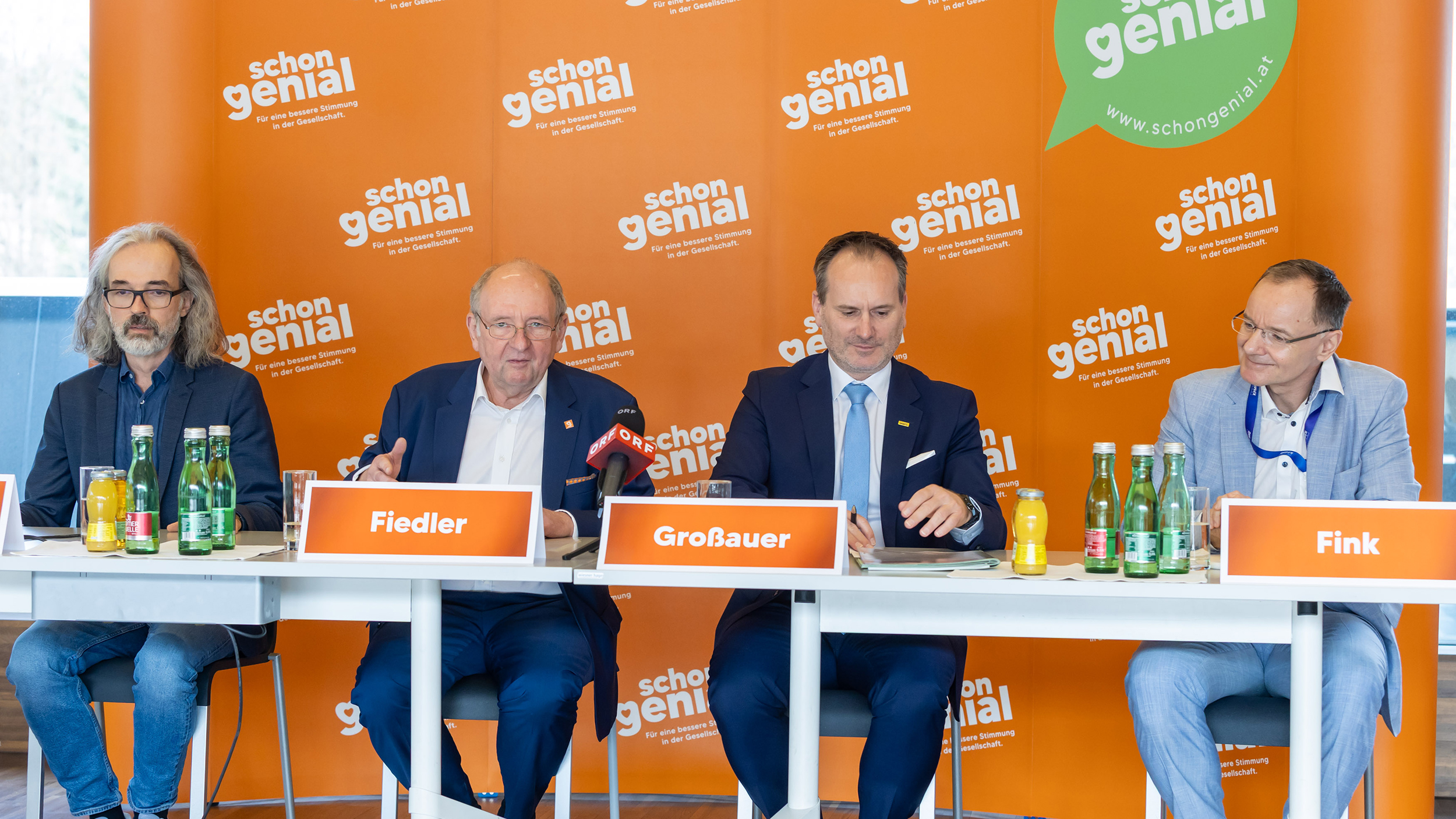 Vier Herren im Anzug sitzen an einem Tisch und geben eine Pressekonferenz