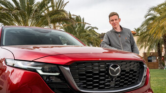 Ein Mann in grauer Weste lehnt an der Motorhaube eines roten Mazda CX-5