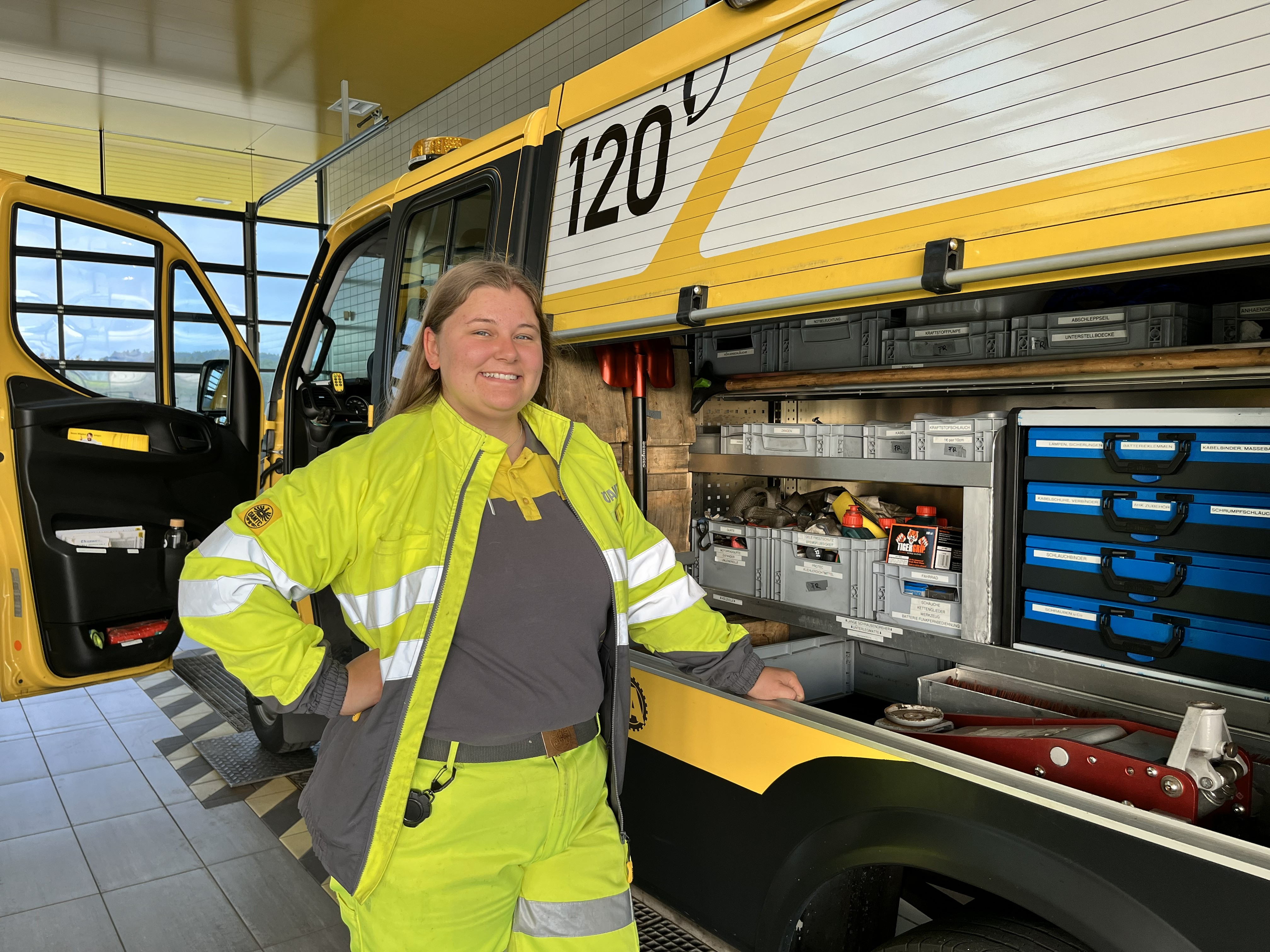 Es ist eine Pannenfahrerin zu sehen, die vor einem geöffnetem Pannenfahrzeug steht.