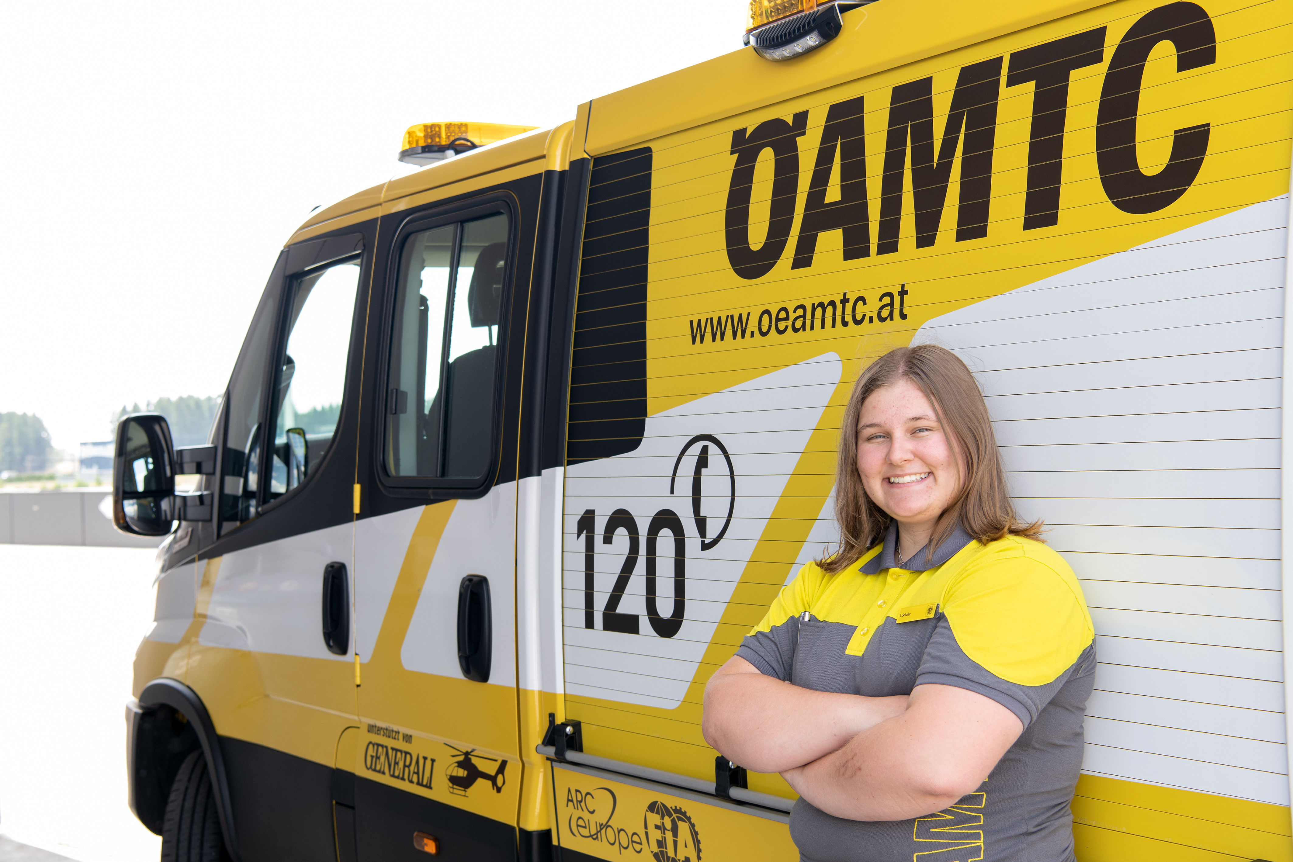 Es ist eine Frau in ÖAMTC-Kleidung zu sehen. Sie lehnt an einem Pannenfahrzeug.