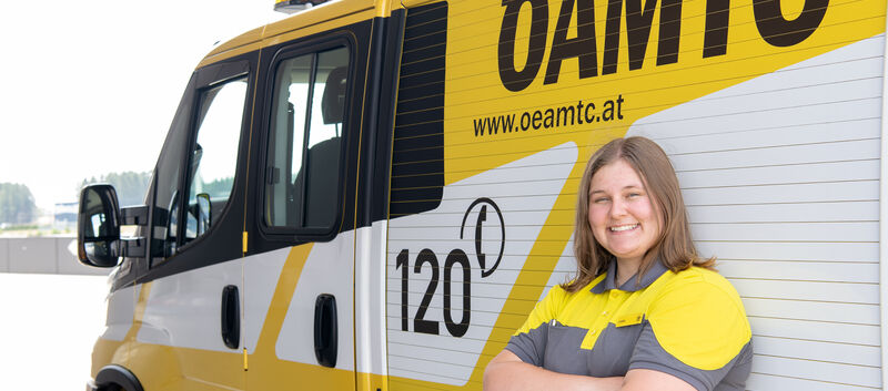 Es ist eine Frau in ÖAMTC-Kleidung zu sehen. Sie lehnt an einem Pannenfahrzeug.