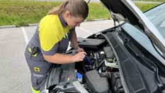 Es ist eine Frau in ÖAMTC-Kleidung zu sehen, die gerade in die geöffnete Motorhaube eines Fahrzeugs schaut.