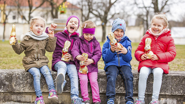 5 Kinder sitzen auf einer Mauer und halten Schokoosterhasen in der Hand auf Schloss Hof.