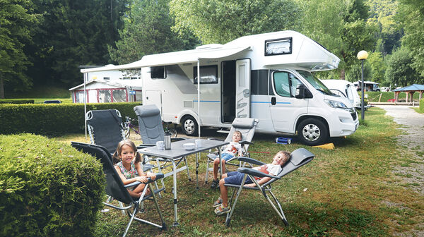 Drei kleine Kinder sitzen am Tisch vor ihrem Wohnmobil.