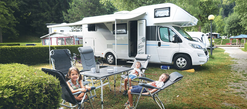 Drei kleine Kinder sitzen am Tisch vor ihrem Wohnmobil.