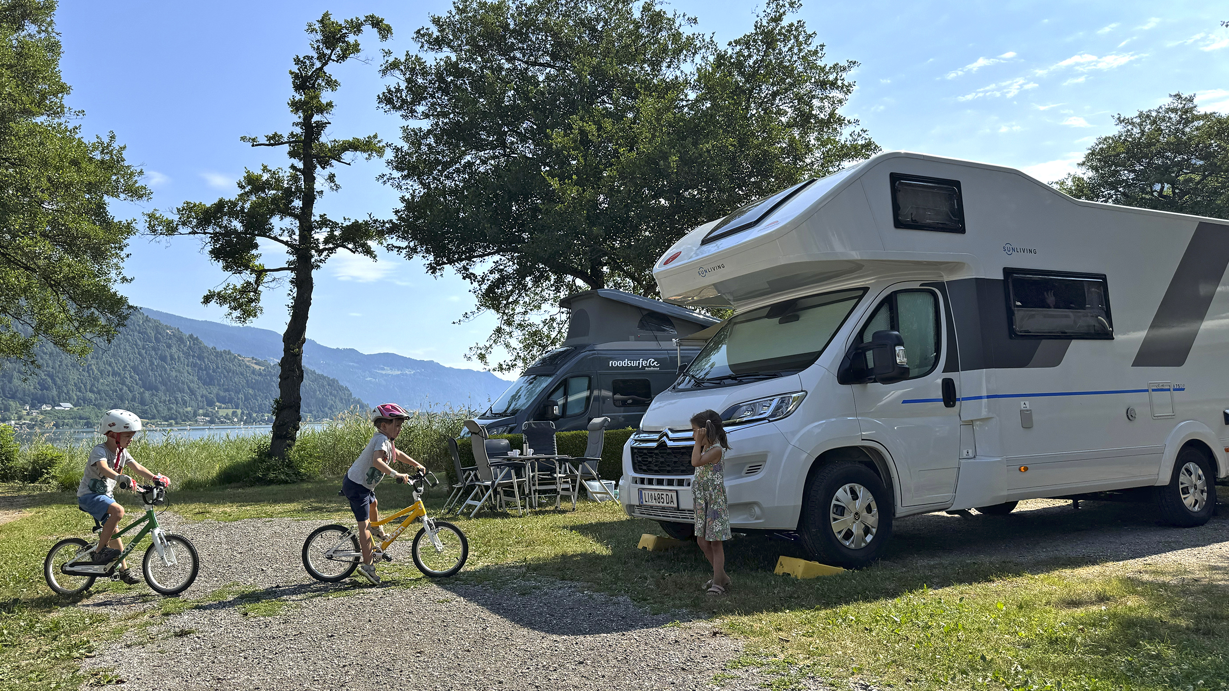 Kinder fahren am Campingplatz vor ihrem Wohnmobil mit ihrem Rad.
