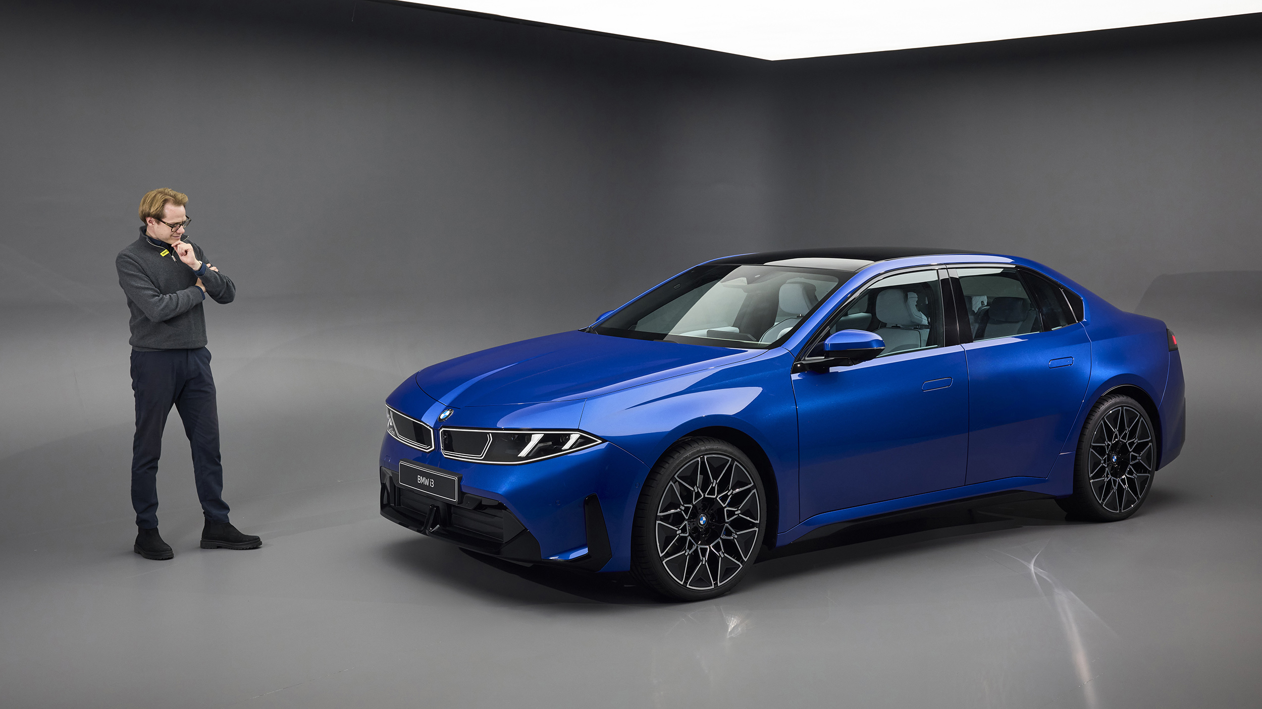 Eine Person steht in einem Studio links neben einer blauen BMW i3 Limousine.