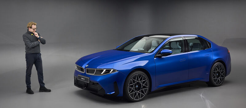 Eine Person steht in einem Studio links neben einer blauen BMW i3 Limousine.