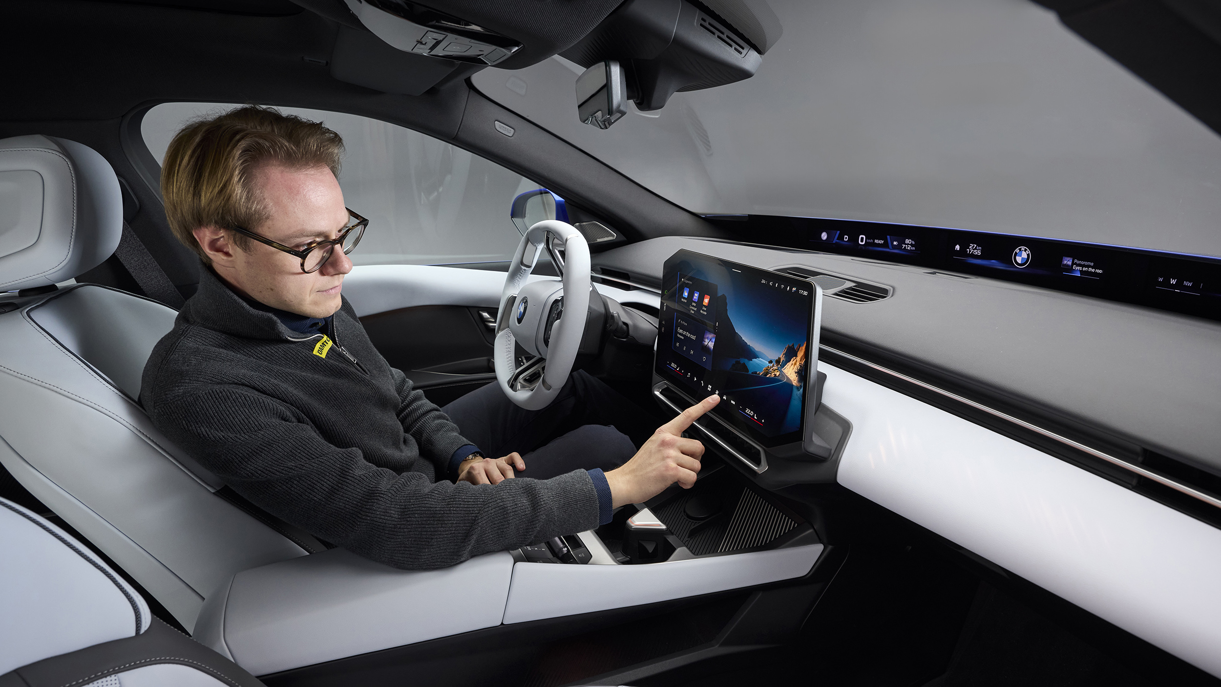 Eine Person sitzt in einem BMW i3 und bedient mit der rechten Hand den Touchscreen.