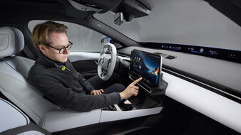 Eine Person sitzt in einem BMW i3 und bedient mit der rechten Hand den Touchscreen.