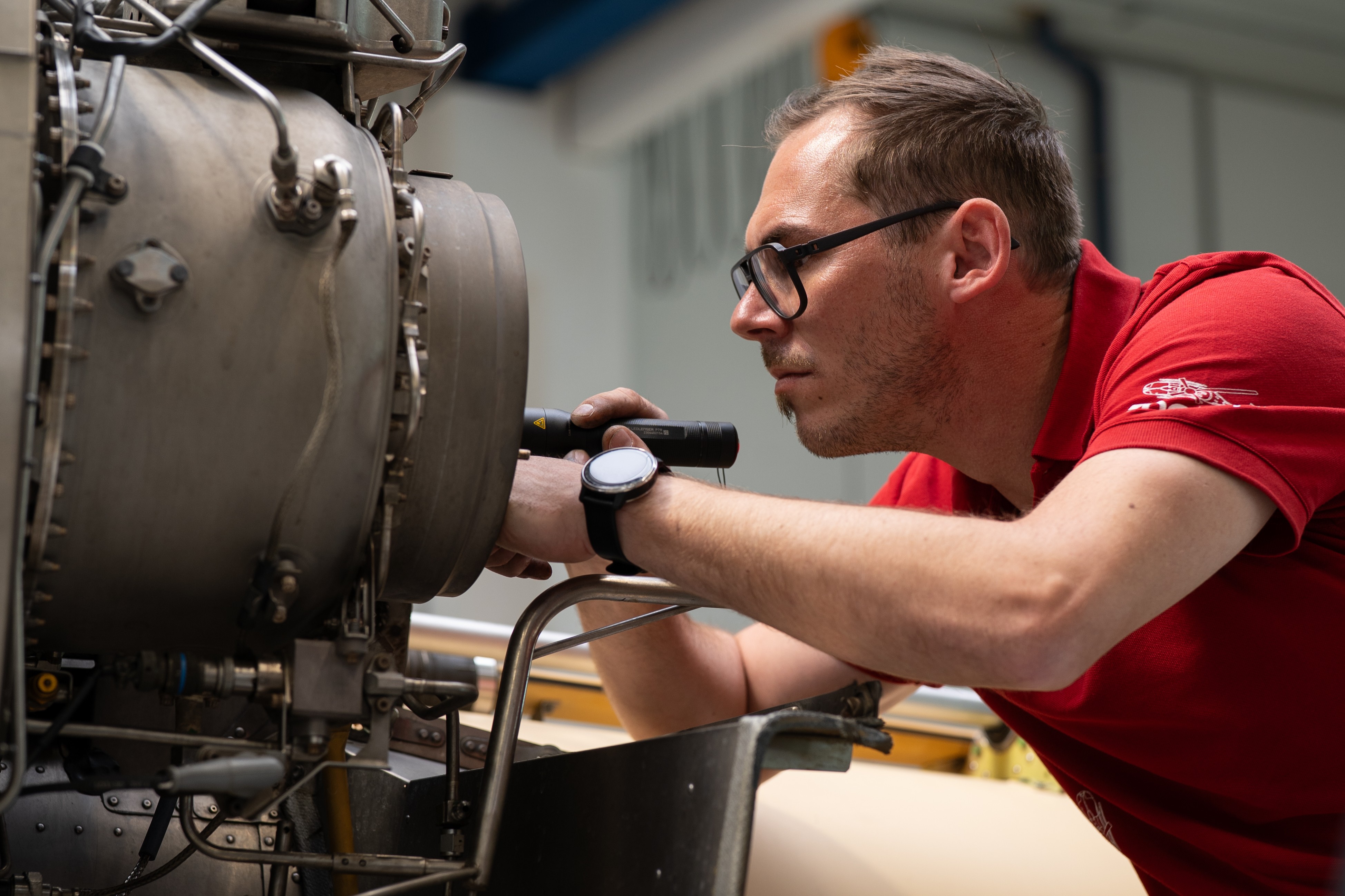Auf dem Bild sieht man einen jungen Mann im roten T-Shirt. er arbeitet gerade an einer Hubschrauber Turbine.
