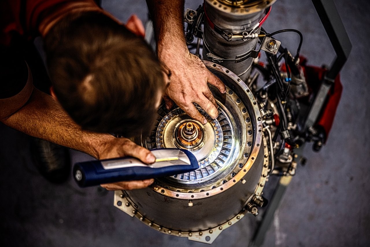 Auf dem Bild sieht man einen jungen Mann, der mit einer Taschenlampe in eine Hubschrauber Turbine leuchtet.