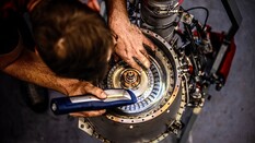 Auf dem Bild sieht man einen jungen Mann, der mit einer Taschenlampe in eine Hubschrauber Turbine leuchtet.