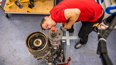 Auf dem Bild sieht man einen jungen Mann im roten T-Shirt, der eine Hubschrauber Turbine inspiziert.
