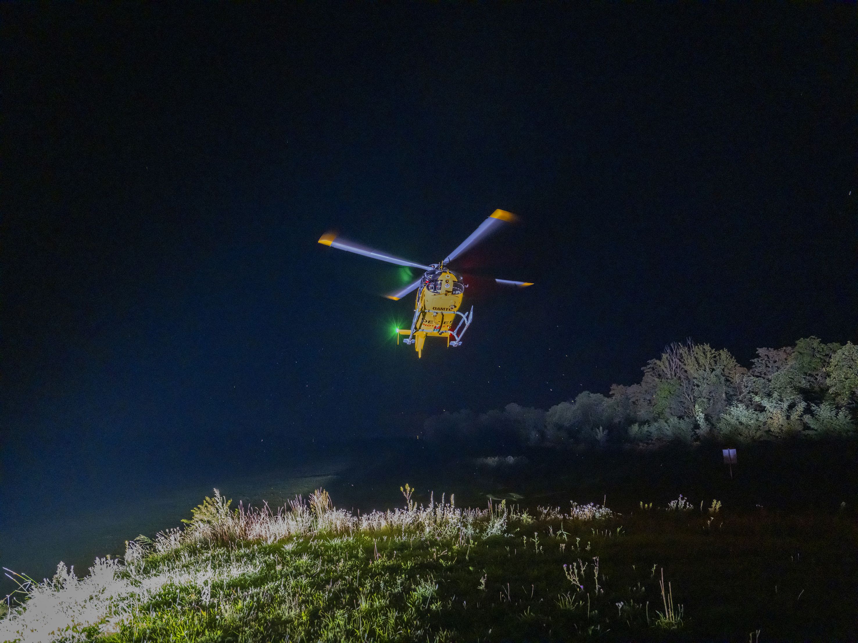 Ein gelber Notarzthubschrauber schwebt nachts über einer grünen Wiese.