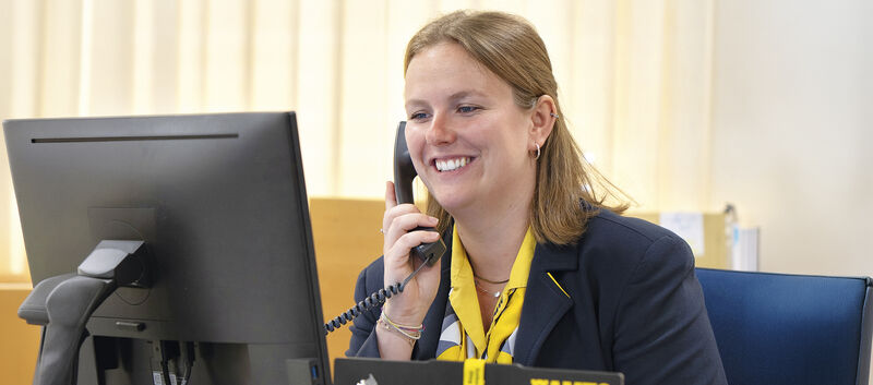 Reisebürokauffrau Katharina Wiesbauer am Telefon, wie sie auf den Computerbildschirm blickt.