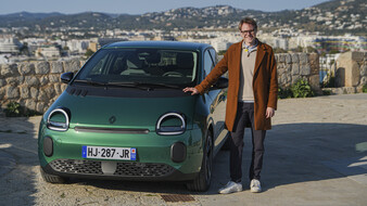 Eine Person im braunen Mantel steht neben einem grünen Renault Twingo.