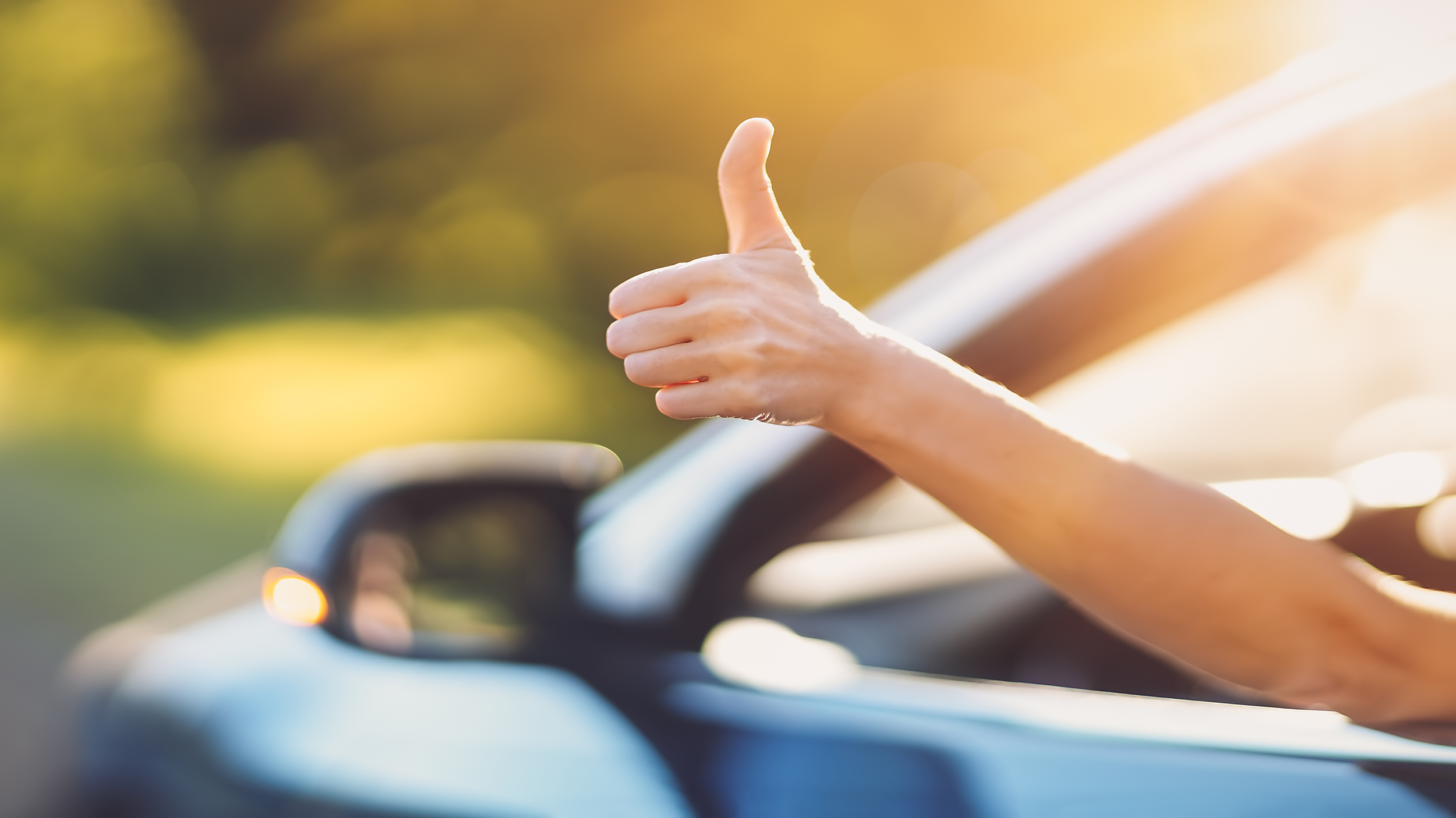 Eine Hand ragt aus einem offenen Autofenster und gibt Daumen hoch.