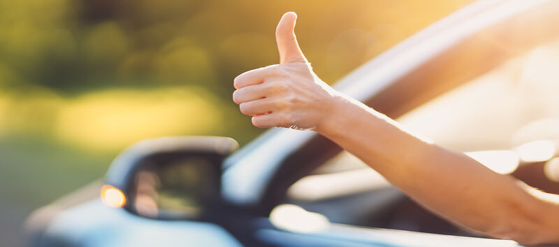 Eine Hand ragt aus einem offenen Autofenster und gibt Daumen hoch.