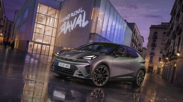 Ein grauer Cupra Raval steht vor einem modernen Gebäude, auf dem ein "Raval"-Schriftzug leuchtet.