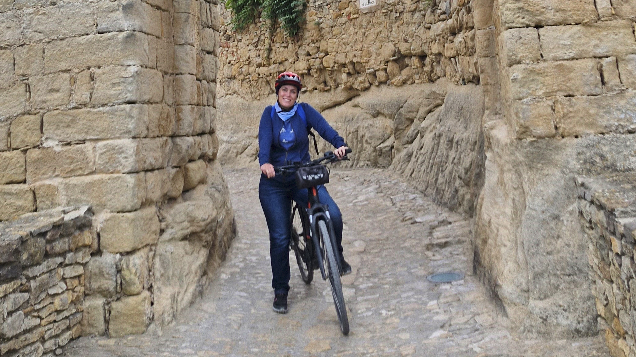 Frau mit Radhelm und Fahrrad steht vor einem Stadttor.