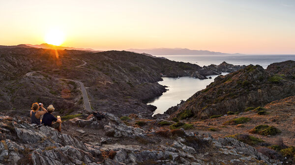 Landschaft am Cap de Creus bei Sonnenuntergang, ein Paar sitzt und blickt aufs Meer.