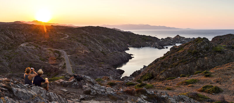 Landschaft am Cap de Creus bei Sonnenuntergang, ein Paar sitzt und blickt aufs Meer.