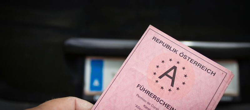 Ein alter rosa Papierführerschein aus Österreich, im Hintergrund ein Nummernschild