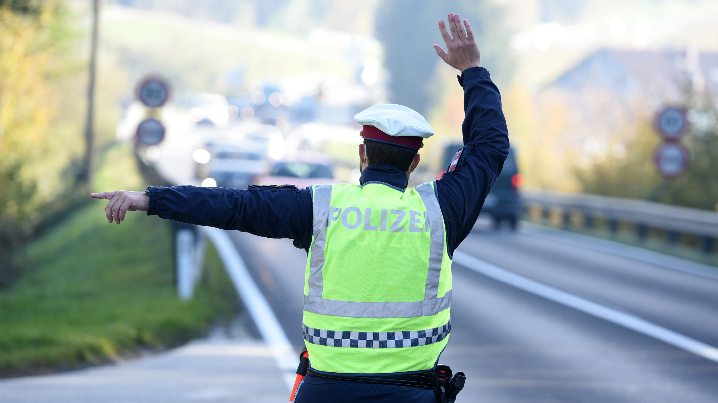 Ein Polizist winkt an einer Straße vorbeifahrende Autos heran