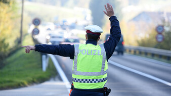 Ein Polizist winkt an einer Straße vorbeifahrende Autos heran