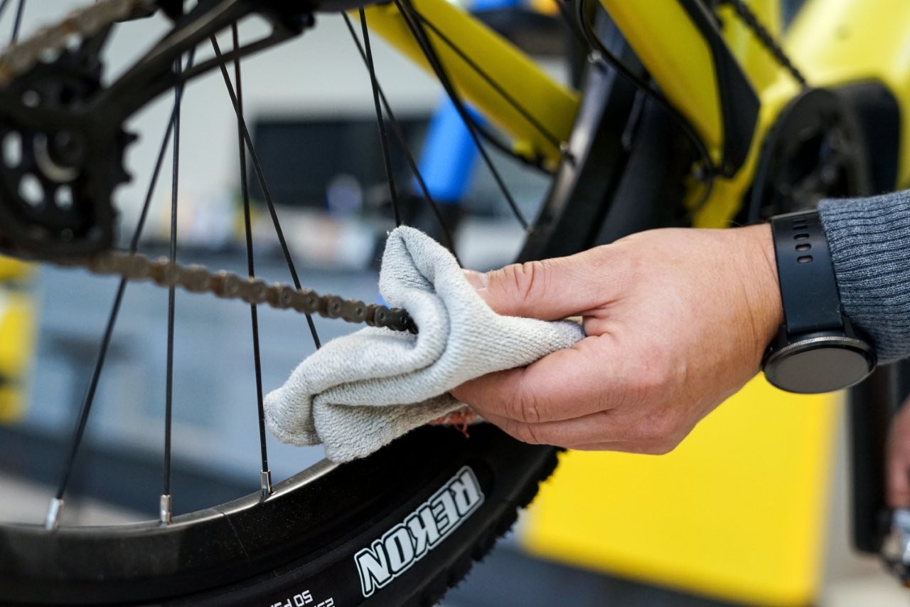  Auf dem Bild sieht man eine Hand mit einem Tuch in der Hand, die eine Fahrradkette pflegt.