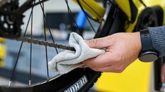 Auf dem Bild sieht man eine Hand mit einem Tuch in der Hand, die eine Fahrradkette pflegt.